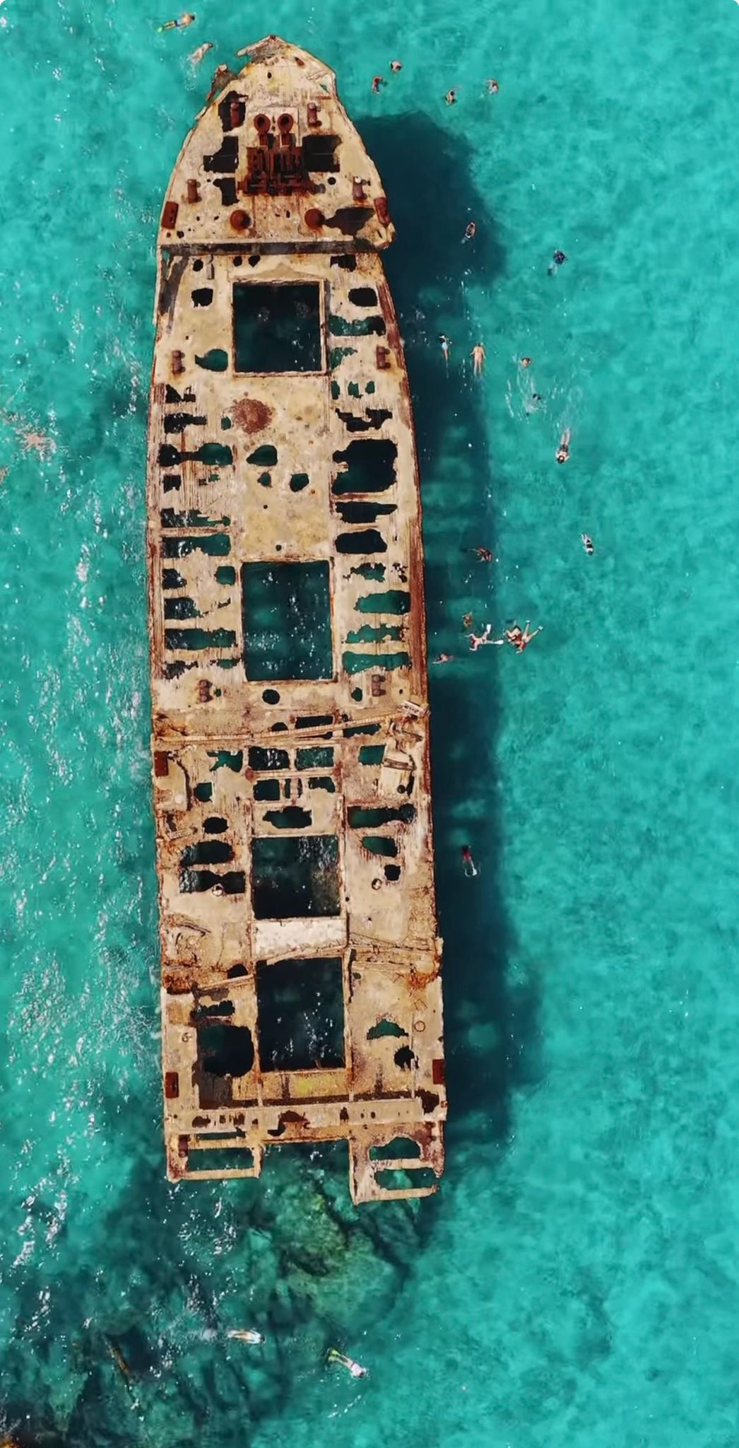 Aerial of a rusted shipwreck with snorkelers in turquoise water